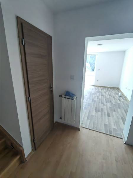 Interiér rodinného domu s dveřmi, radiátorem a podlahou s dřevěným dekorem.