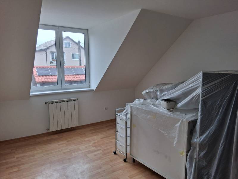 Místnost v rodinném domě s oknem, topným tělesem a podlahou s dřevěným dekorem.