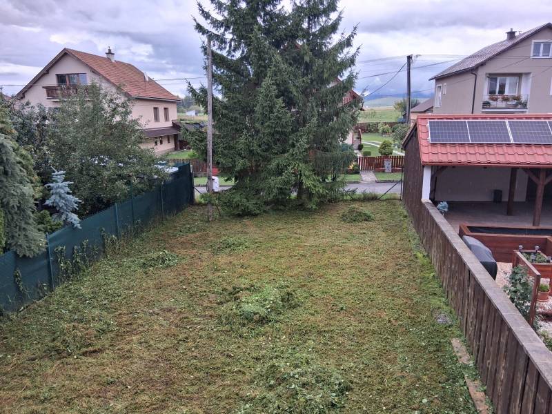 Zahrada u rodinného domu v Ľubeli s udržovaným trávníkem a hustými stromy.