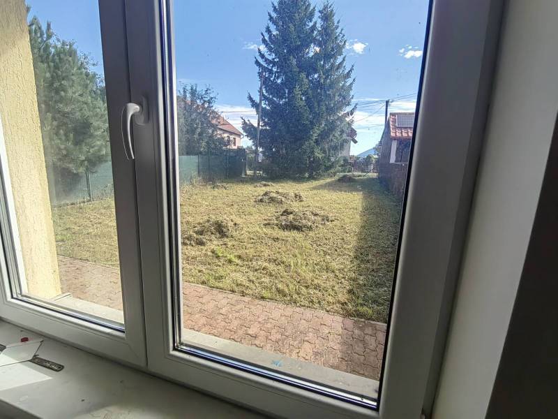 Pohled z rodinného domu v Ľubeli do zahrady s udržovaným trávníkem a stromy.