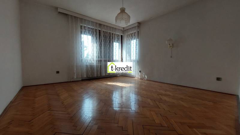 Prostorný pokoj s podlahou s dřevěným dekorem, bílými stěnami a záclonami v rodinném domě.