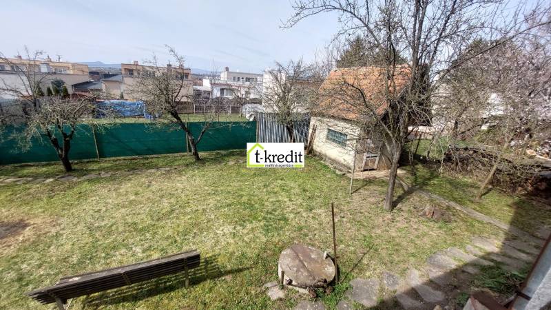 Zahrada rodinného domu ve Zlatých Moravcích s trávníkem, stromy a lavičkou.