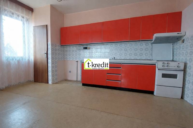 Kuchyně s červenými skříňkami, sporákem a oknem v rodinném domě.