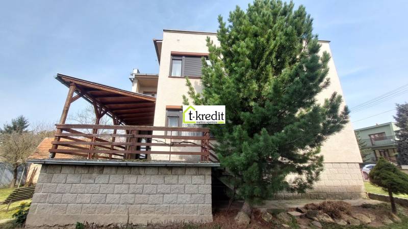 Rodinný dům ve Zlatých Moravcích s dřevěnou terasou, vysokým stromem a zahradou.