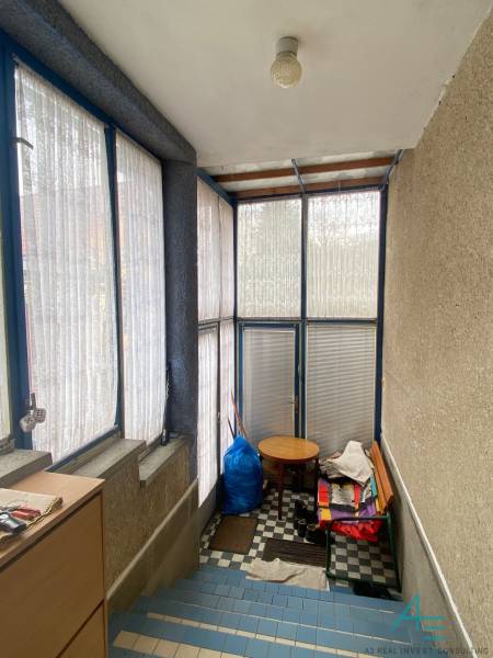 Prosklená veranda s modrým rámováním, šachovnicová podlaha a jednoduchý nábytek.