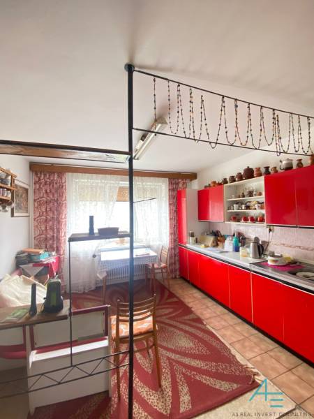 Červená kuchyňská linka v rodinném domě s dekorativním závěsem a puntíkovaným kobercem.