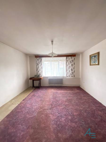 Pokoj v rodinném domě s fialovým kobercem, květinovými závěsy a lustrem.