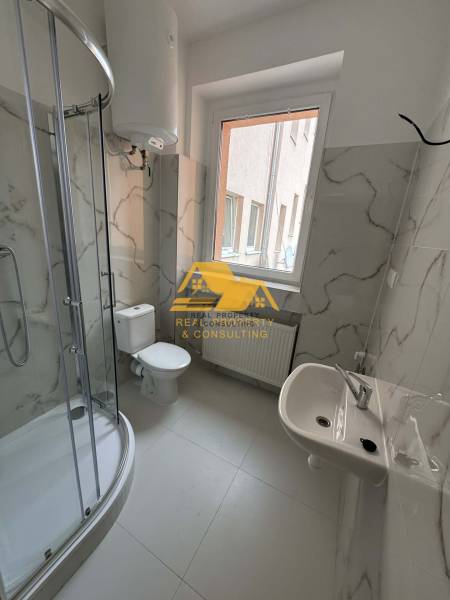 Koupelna v 1-pokojovém bytě s rohovým sprchovým koutem a keramickými obklady.