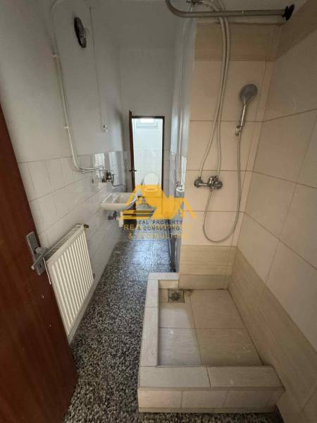 Koupelna v garsonce s jednoduchým sprchovým koutem, umyvadlem a kachličkami.