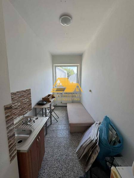 Malá garsonka s umyvadlem, stolem a lehátkem, vhodná pro praktické bydlení.