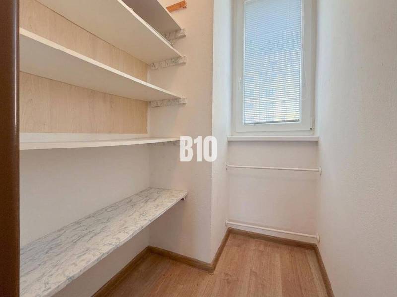 Malý pokoj v rekreačním apartmánu s policemi a oknem, podlaha s dřevěným dekorem.