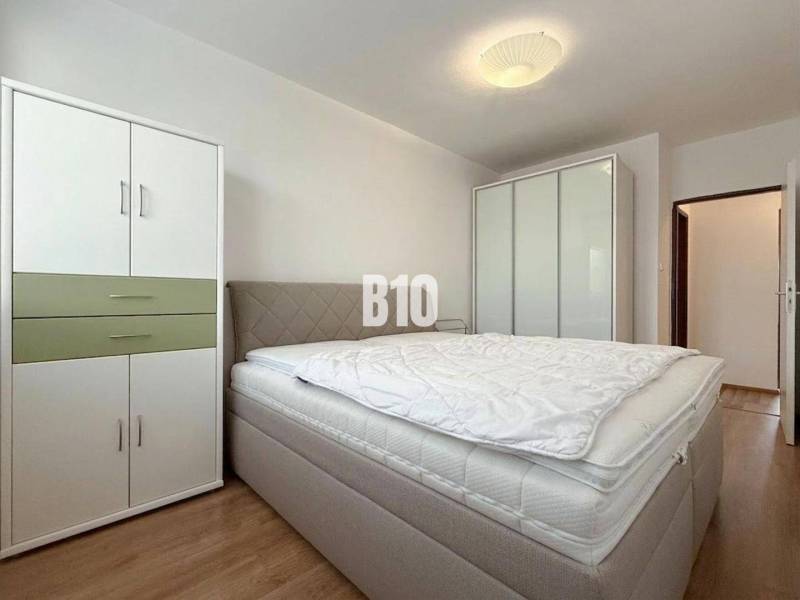 Světlý pokoj v rekreačním apartmánu s postelí, šatníkovými skříněmi a podlahou s dřevěným dekorem.