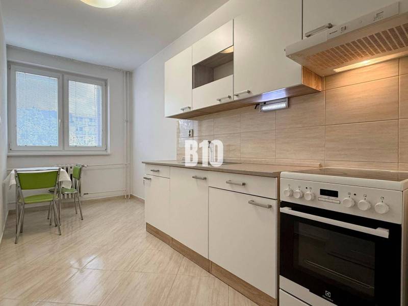 Světlá kuchyně v Rekreačním apartmánu s sporákem a stolem se zelenými židlemi.