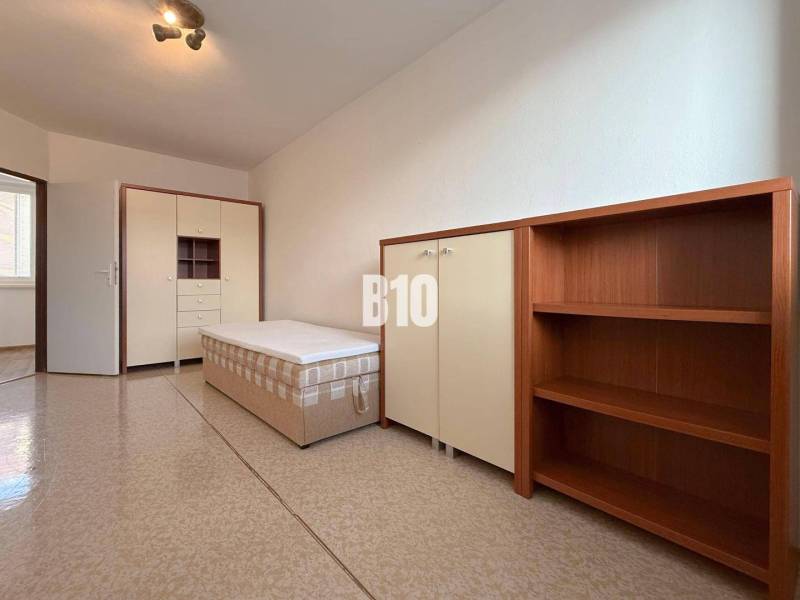 Světlá místnost v Rekreačním apartmánu s postelí, skříní a policovou sestavou.