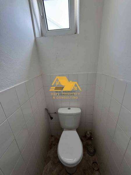 Kompaktní toaleta s oknem, bílé dlaždice, podlaha s dřevěným dekorem.