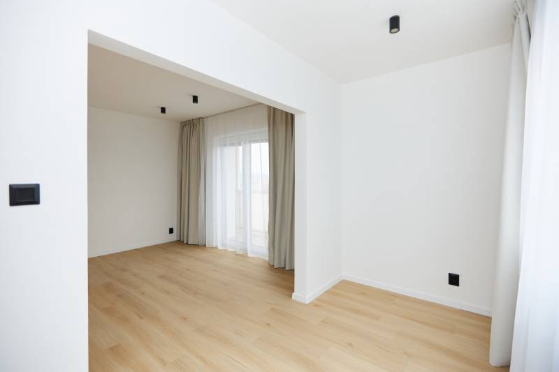 Pokoj v 3-pokojovém bytě s podlahou s dřevěným dekorem, závěsy a francouzským oknem.