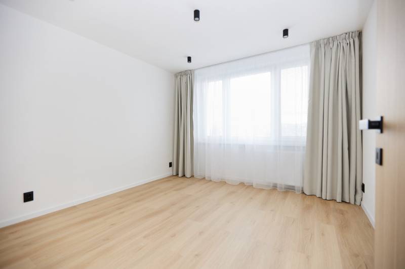 Prázdný pokoj s oknem, závěsy a podlahou s dřevěným dekorem ve 3pokojovém bytě.