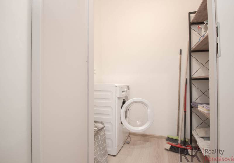 Prádelna v 3-pokojovém bytě s pračkou, regálem a čisticími potřebami.