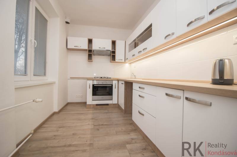 Kuchyně se spotřebiči, bílými skříňkami a podlahou s dřevěným dekorem v 2-pokojovém bytě.