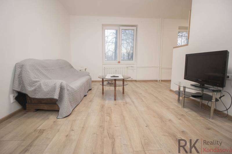 Obývací pokoj v 2-pokojovém bytě s pohovkou, stolkem a televizí na podlaze s dřevěným dekorem.