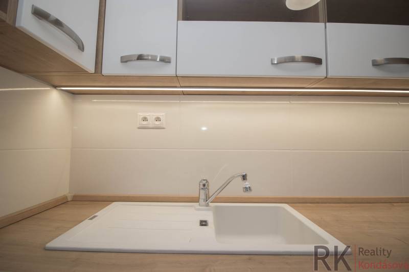 Kuchyňská pracovní deska s dřevěným dekorem a bílým dřezem v 2-pokojovém bytě.