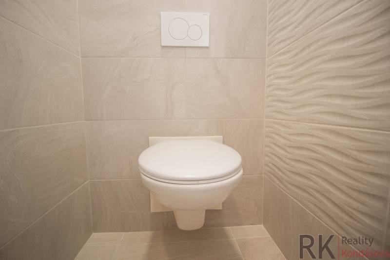 Koupelna v 2-pokojovém bytě s bílou toaletou a světlými obklady.