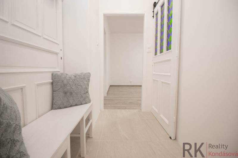 Světlá chodba s bílým nábytkem a dekorativními polštáři v 2pokojovém bytě.