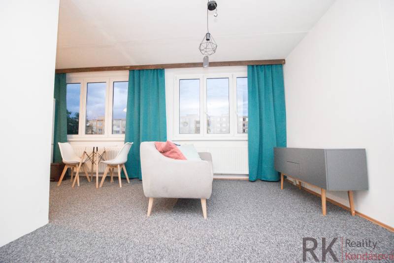 Obývací pokoj ve 4pokojovém bytě s modrými závěsy a šedým nábytkem.