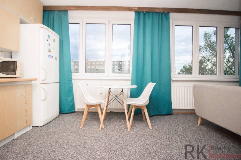 Kuchyně se stolem a židlemi ve 4pokojovém bytě, skříň a okna s tyrkysovými závěsy.