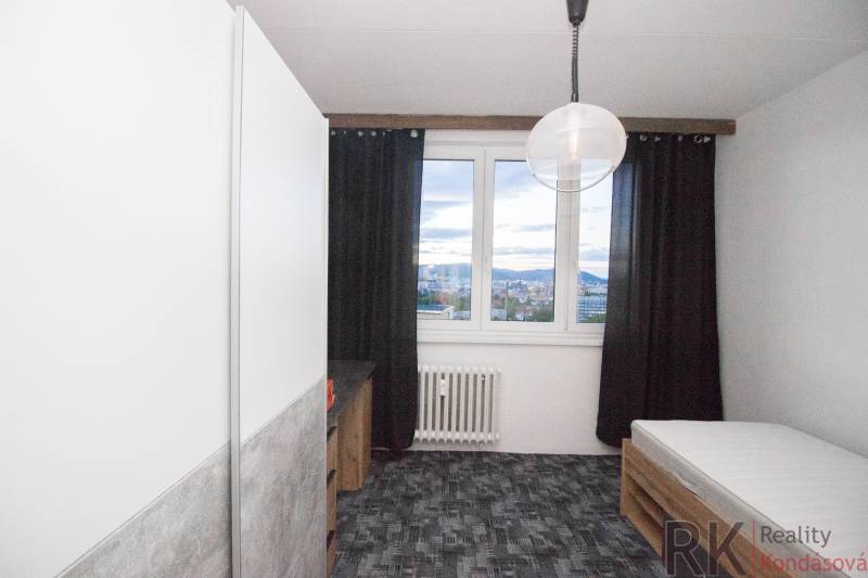 Pokoj ve 4pokojovém bytě s postelí, tmavými závěsy a výhledem z okna.