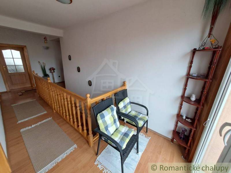 Interiér rodinného domu se schodištěm, židlemi a podlahou s dřevěným dekorem.