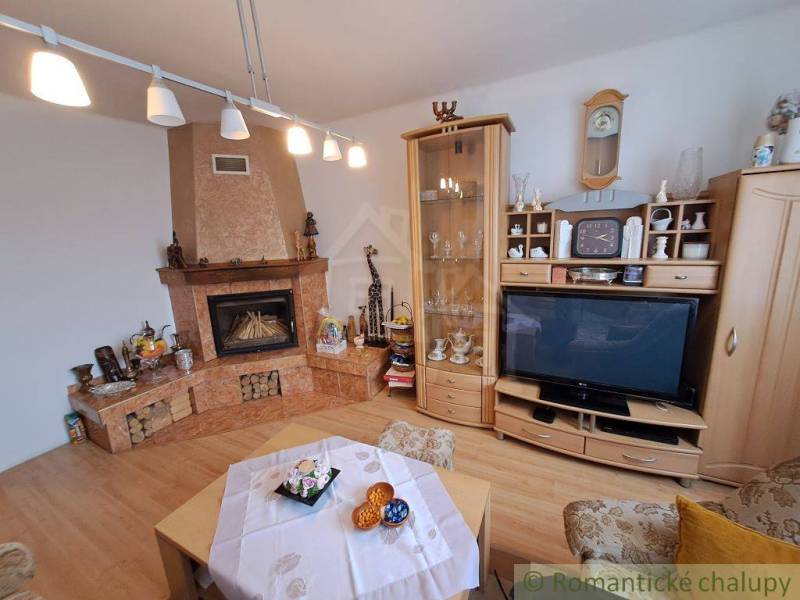 Obývací pokoj v rodinném domě s krbem, dřevěným dekorem podlahy a vitrínou.