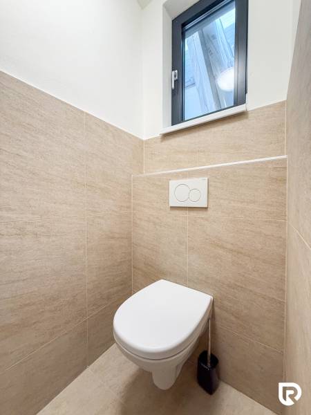 Toaleta s přírodním obkladem v obchodních prostorech, jednoduchý design a oknem.