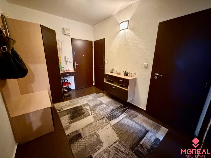 Předsíň s tmavými dveřmi, komodou a podlahou s dřevěným dekorem ve 3-pokojovém bytě.