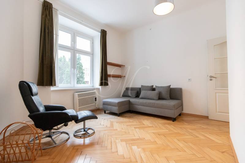 Světlý obývací pokoj s podlahou s dřevěným dekorem ve 4-pokojovém bytě, šedá sedačka, křeslo.