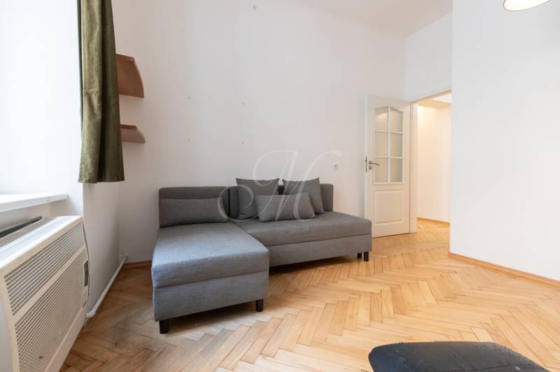 Šedá pohovka s polštáři a podlaha s dřevěným dekorem ve 4-pokojovém bytě.