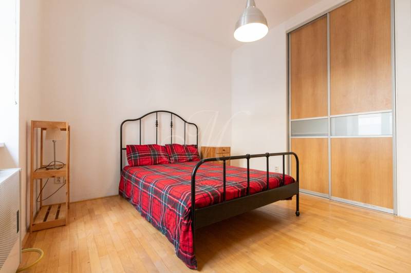 Ložnice ve 4pokojovém bytě s kovovou postelí, šatní skříní a podlahou s dřevěným dekorem.