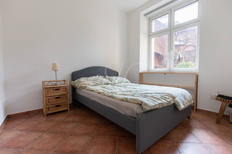 Ložnice ve 4pokojovém bytě s postelí, nočním stolkem a velkým oknem.