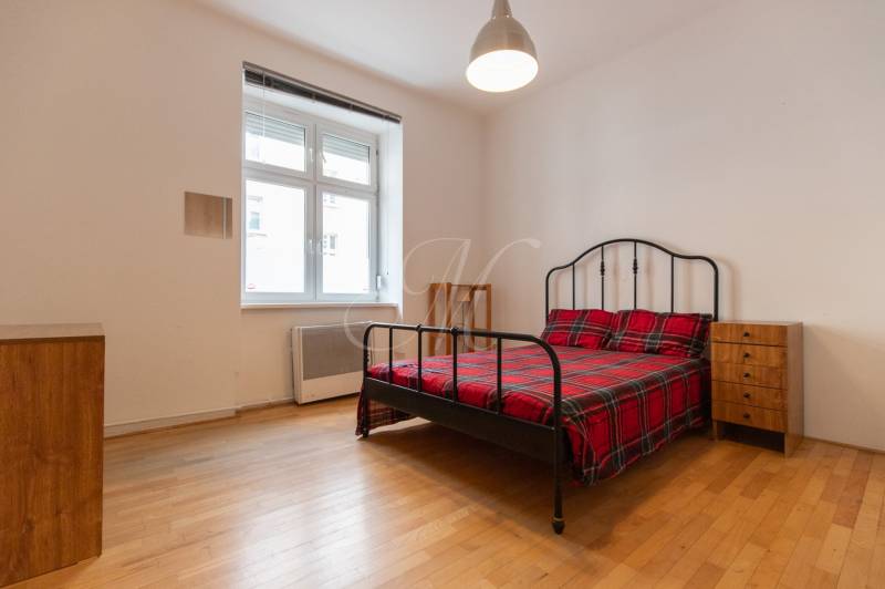 Ložnice ve 4pokojovém bytě s postelí, nočními stolky a podlahou s dřevěným dekorem.