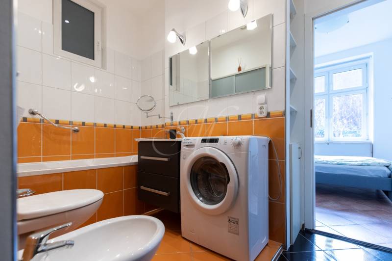Koupelna s vestavěnou pračkou a oranžovým obkladem ve 4-pokojovém bytě.