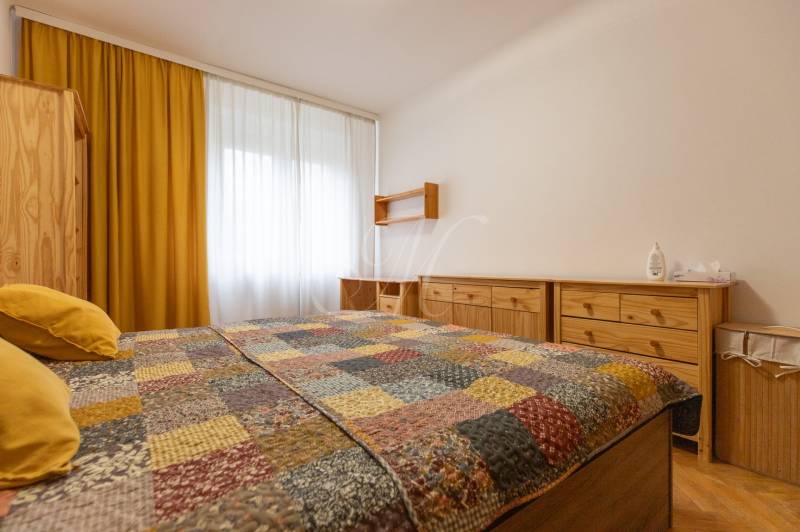 Ložnice v dvoupokojovém bytě se žlutými závěsy a dřevěným nábytkem.