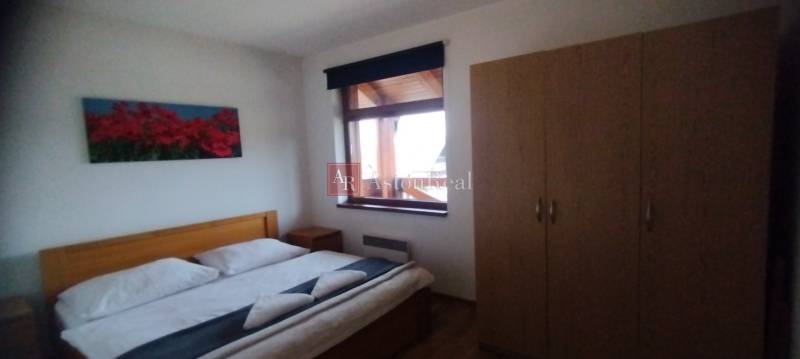 Ložnice s manželskou postelí, podlahou s dřevěným dekorem a šatní skříní v 2pokojovém bytě.