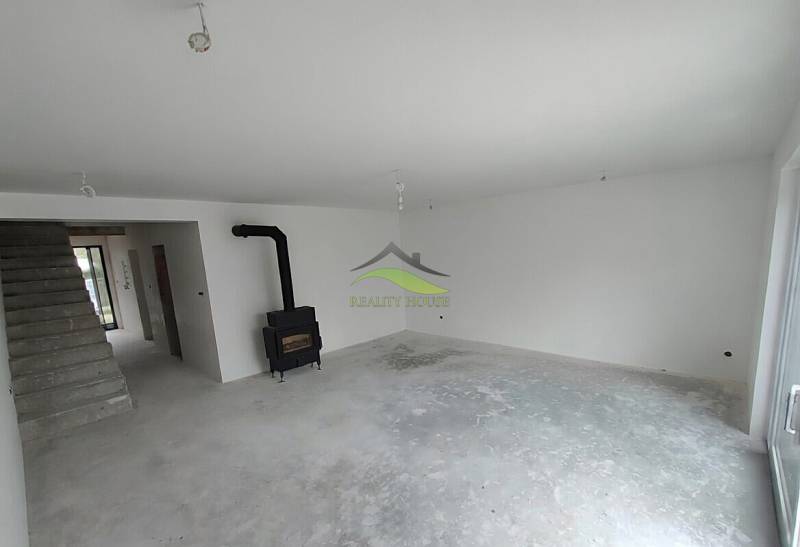 Interiér rodinného domu s krbem a schodištěm, čekající na dokončení.