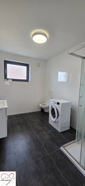 Koupelna ve 3-pokojovém bytě se sprchovým koutem, pračkou a černou dlažbou.