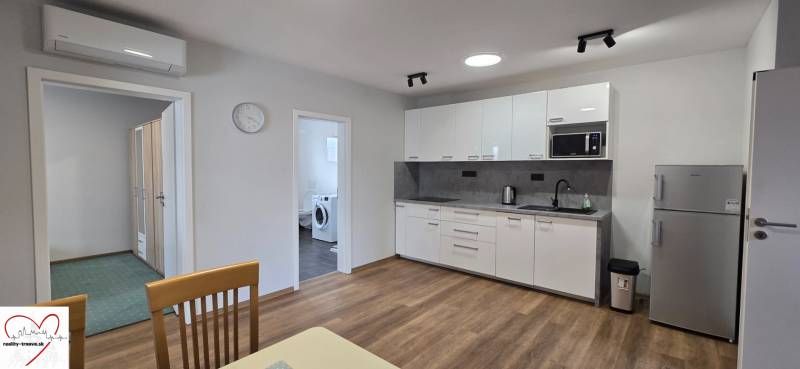 Kuchyně s bílými skříněmi a spotřebiči v 3-pokojovém bytě, podlaha s dřevěným dekorem.