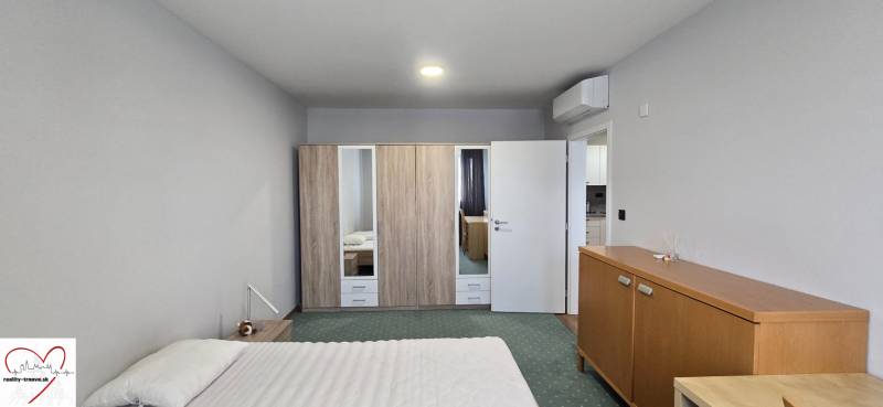Pokoj v 3-pokojovém bytě s postelí, skříní, klimatizací a dřevěným dekorem nábytku.