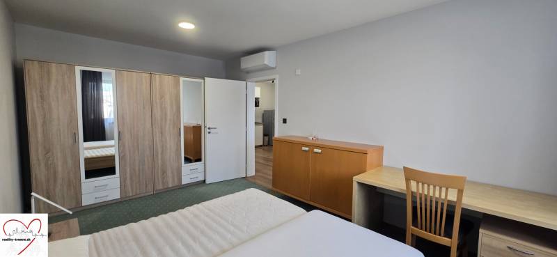 Ložnice v třípokojovém bytě s manželskou postelí, skříní a stolem.