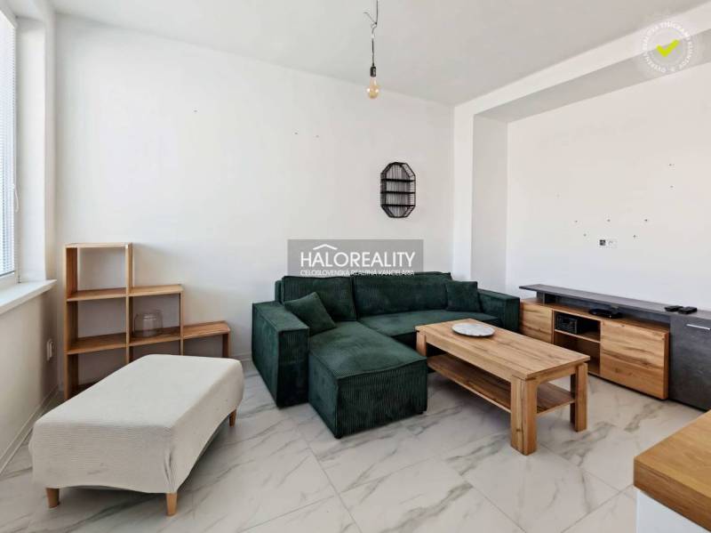 Obývací pokoj s tmavou pohovkou v 3pokojovém bytě s dlažbovou podlahou a dřevěným dekorem nábytku.