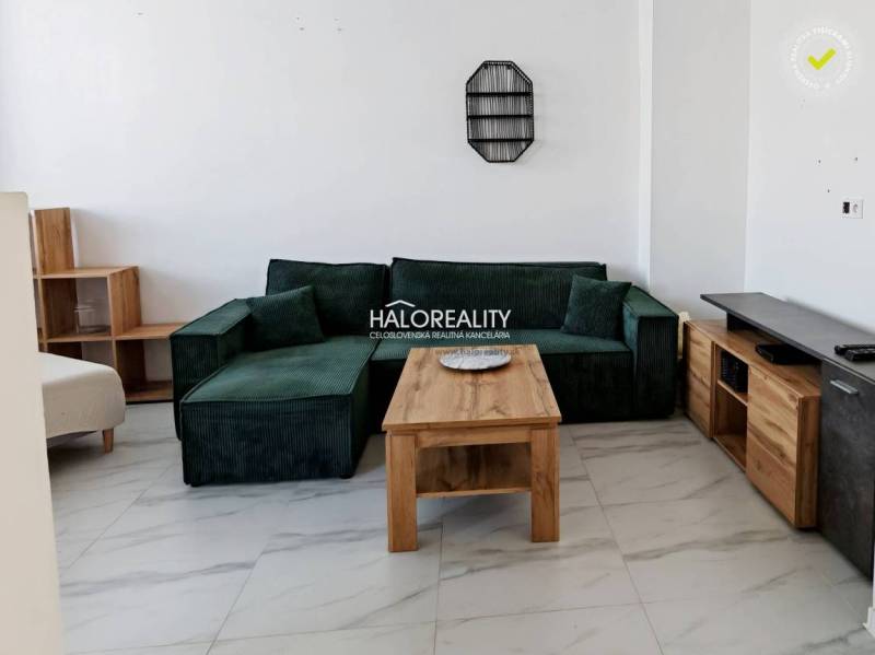 Obývací pokoj v 3-pokojovém bytě se zelenou sedačkou a dřevěným stolem.