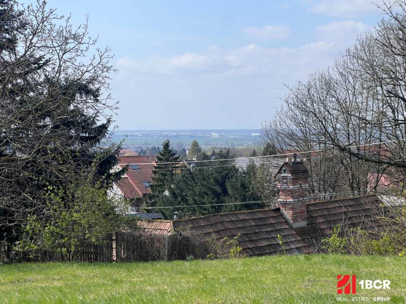Zahrady s výhledem mezi stromy a střechami na Budovatelské ulici, Marianka, Pozemky - bydlení.